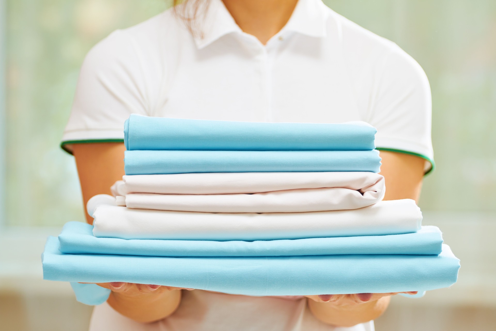 Closeup of woman's hand holding a stack of clean folded bed sheets of blue and white colors. Blurred background.